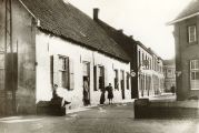 Kerkstraat. Links pand Kuenen-Bosmans, vervolgens café van den Akker, vervolgens bakkerswinkel, vervolgens Jan Jansen textiel (fietsen) en zijgevel van Johan van Roessel. Op het muurtje zit de oudste zoon van H. Wouters van "de Zwaan". Voor meer details klik hier.