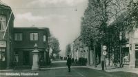 Hoofdstraat met links de pomp met daarvoor de veldwachter Huub van Osch. Links daarachter de levensmiddelenwinkel van Hovenier Spar. Op de achtergrond het pand van Bosmans sanitair, loodgieter en electra. Rechts de winkel van Van Liempd-Mallens. Voor meer details klik hier.